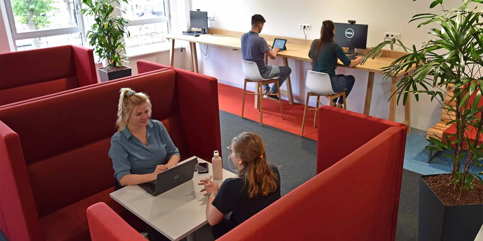 Vier collega's in een ruimte, twee zijn op de voorgrond in gesprek